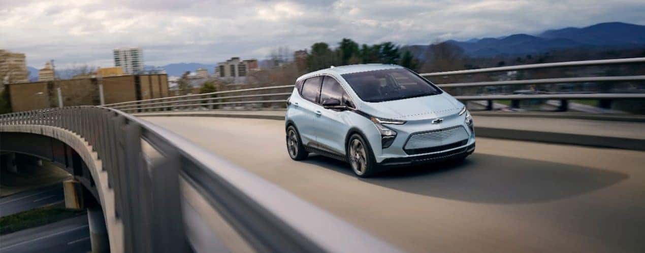 A light blue 2023 Chevy Bolt EV is shown driving on a bridge.