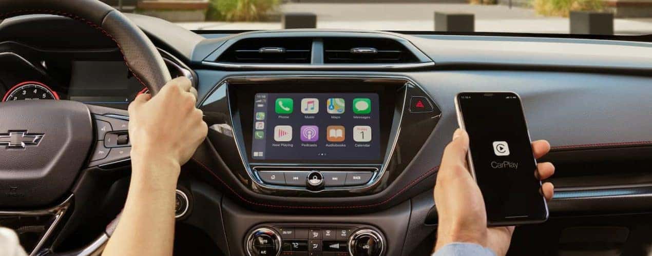 A person is shown holding a cellphone near the infotainment screen in a 2023 Chevy Trailblazer.