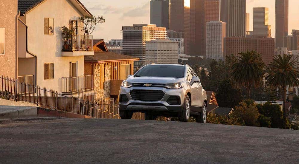 A silver 2022 Chevy Trax is shown driving up a city hill.