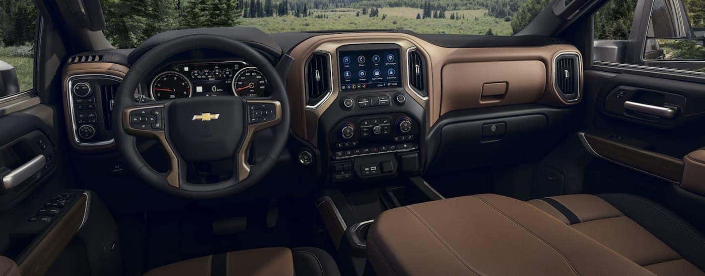 The black and brown interior of a 2023 Chevy Silverado 2500 HD shows the steering wheel and infotainment screen.
