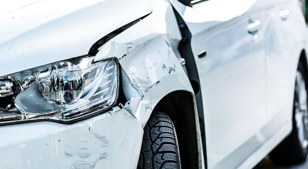 A white car is shown from the front with damage to the front fender.