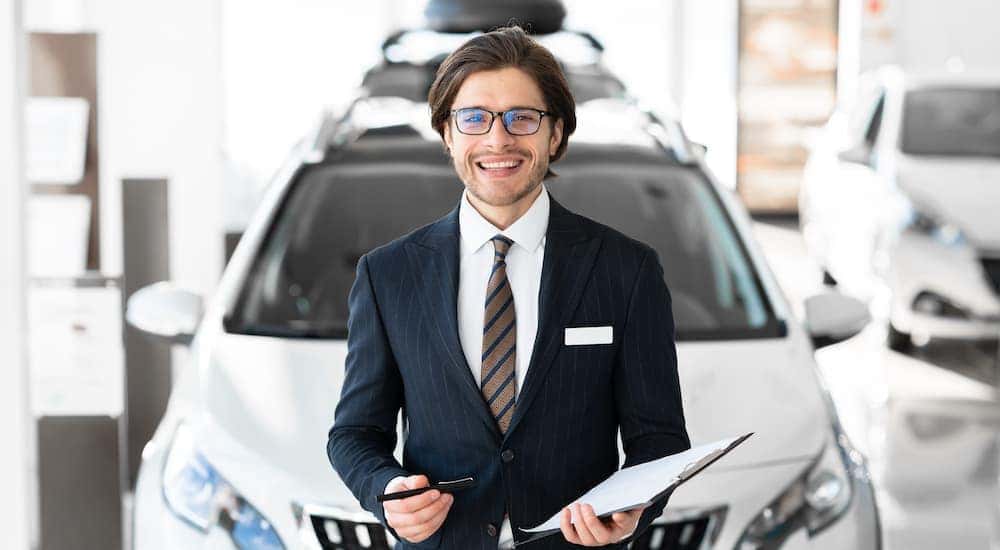 A salesman is shown standing in front of a white car.