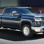 A blue 2023 Chevy Silverado 2500 is shown towing an antique car.