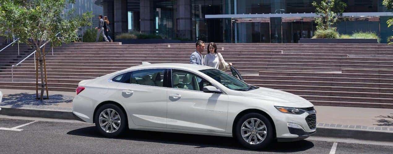 A white 2022 Chevy Malibu is shown from the side on the side of a city street.
