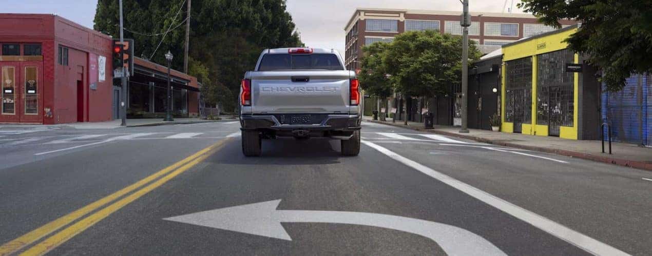A siler 2023 Chevy Colorado is shown from behind while in a turning lane.