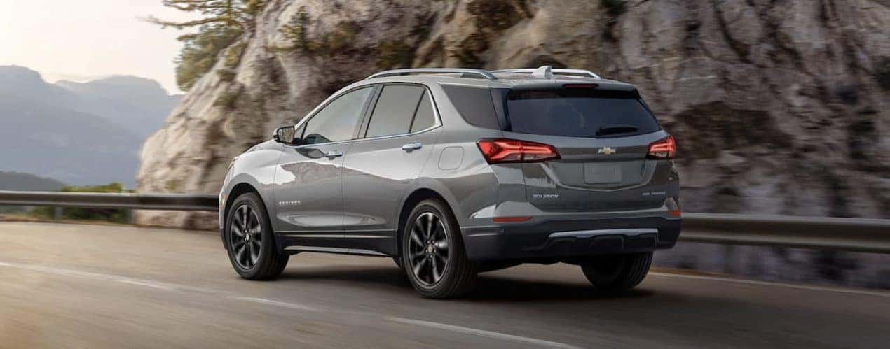 A grey 2023 Chevy Equinox is shown from the rear driving on an open road.