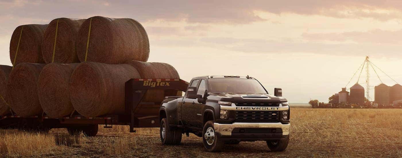 A black 2022 Chevy Silverado 3500 HD is shown parked in a field towing a trailer full of hay.
