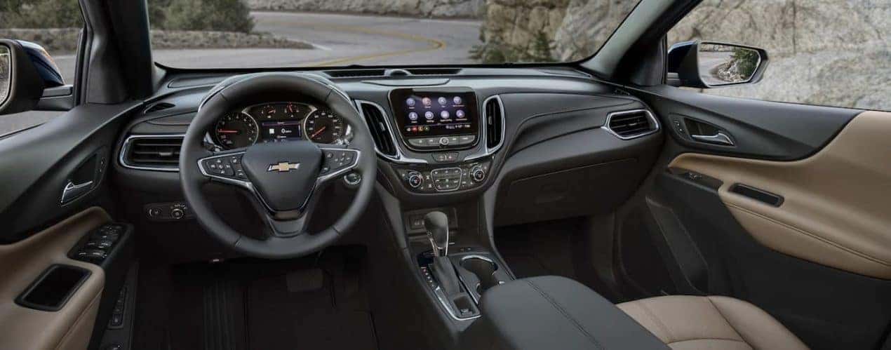 The grey interior of a 2023 Chevy Equinox shows the steering wheel and infotainment screen.
