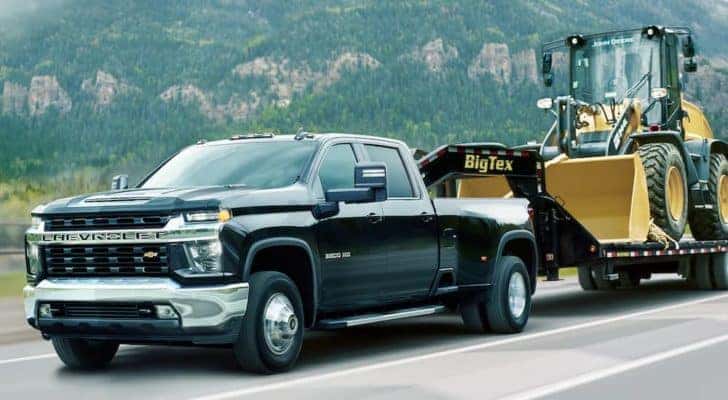 A black 2021 Chevy Silverado 3500HD is shown towing heavy machinery.