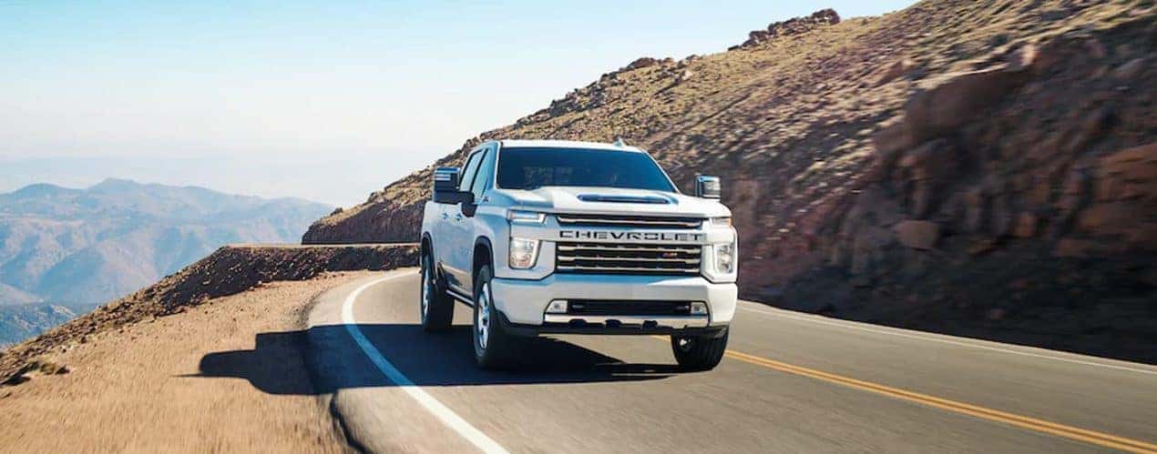 A white 2023 Chevy Silverado HD Z71 is shown driving on a mountain highway.