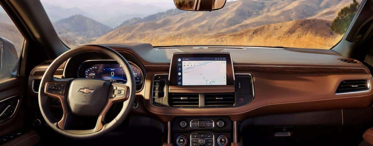 The brown interior of a 2023 Chevy Tahoe shows the steering wheel and infotainment screen.