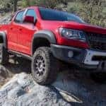A red 2019 Chevy Colorado ZR2 Bison is shown from the front at an angle while driving over a rock.