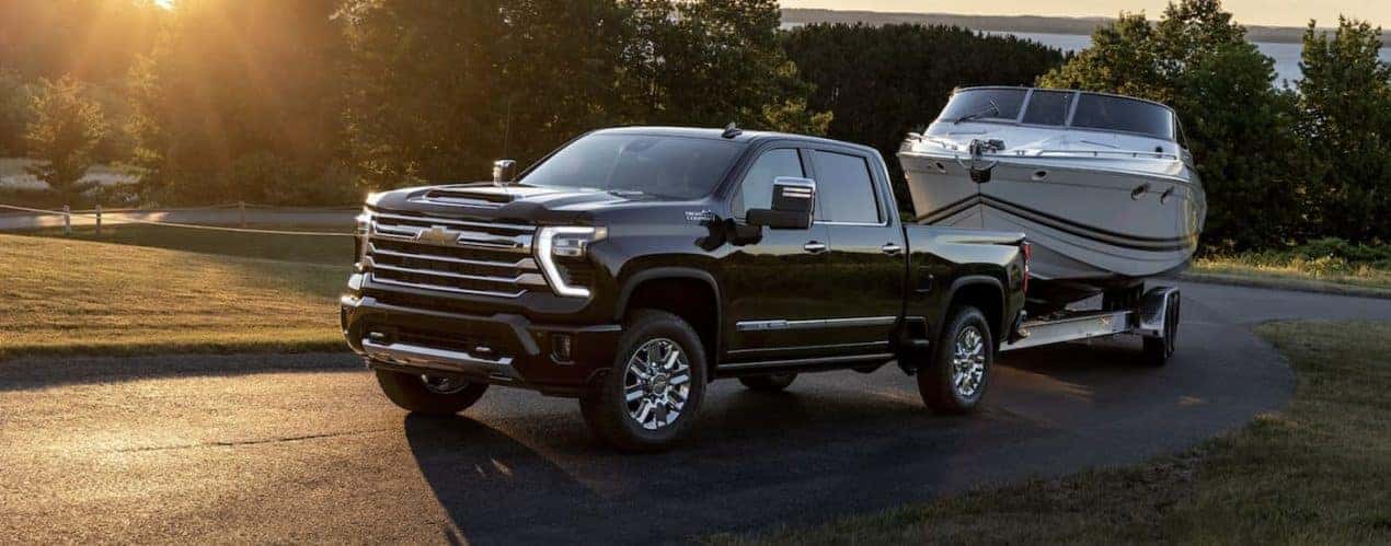 A black 2024 Chevy Silverado 2500 HD is shown towing a boat on an open road.