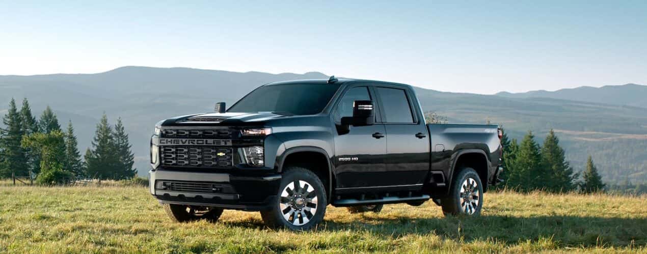 A black 2023 Chevy Silverado 2500 HD Custom is shown parked in an open field.
