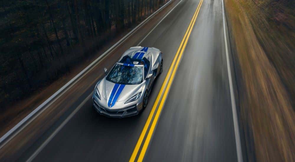 A silver 2024 Chevy Corvette E-Ray 3LZ is shown from high angle on a tree-lined road after looking electric vehicles for sale.