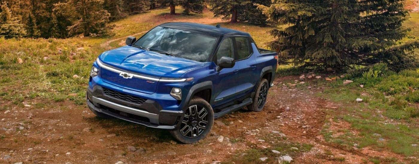 A blue 2024 Chevy Silverado EV RST is shown parked in a clearing.