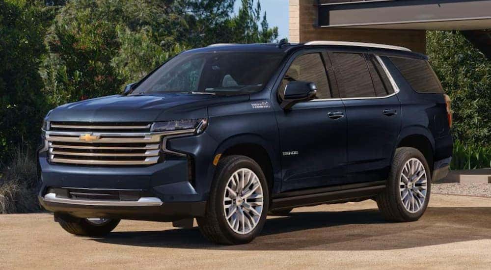 A popular Chevy Tahoe for sale, a blue 2023 Chevy Tahoe, is shown from the side parked in front of a house.