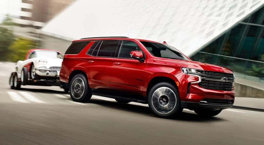 A red 2023 Chevy Tahoe is shown towing an antique vehicle.
