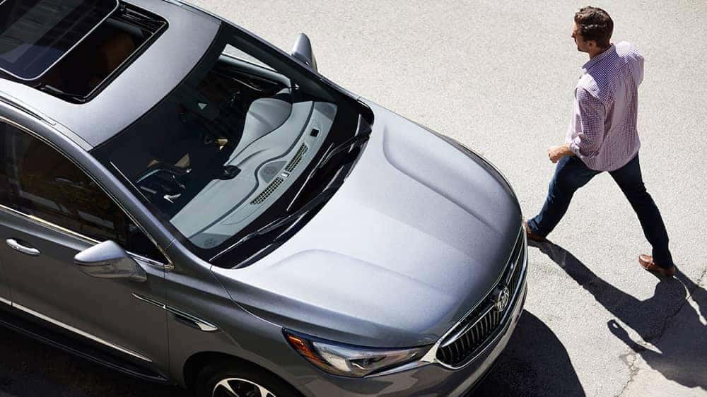 Skyview of a man in a plaid shirt walking toward his silver 2019 Buick Enclave
