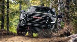 A black 2022 GMC Sierra 1500 AT4 is shown off-roading in the woods.