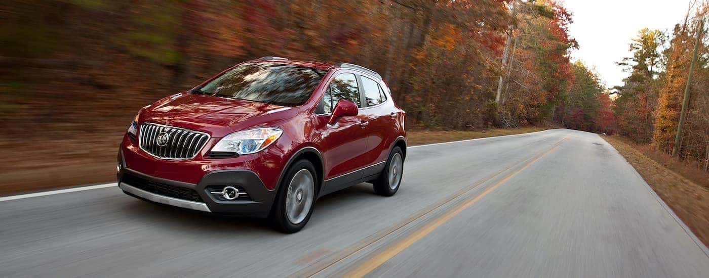 A red 2013 Buick Encore is shown driving on a tree-lined road.