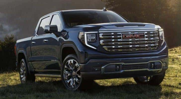 A blue 2023 GMC Sierra 1500 Denali is shown parked in a grass field.