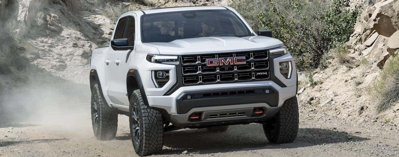 A white 2023 GMC Canyon AT4X is shown off-roading on a dusty trail.