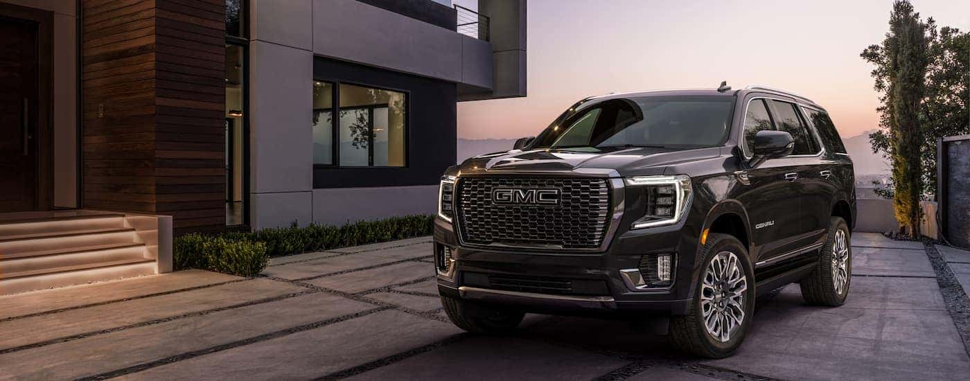A black 2023 GMC Yukon Denali Ultimate is shown parked in a driveway next to grey house.