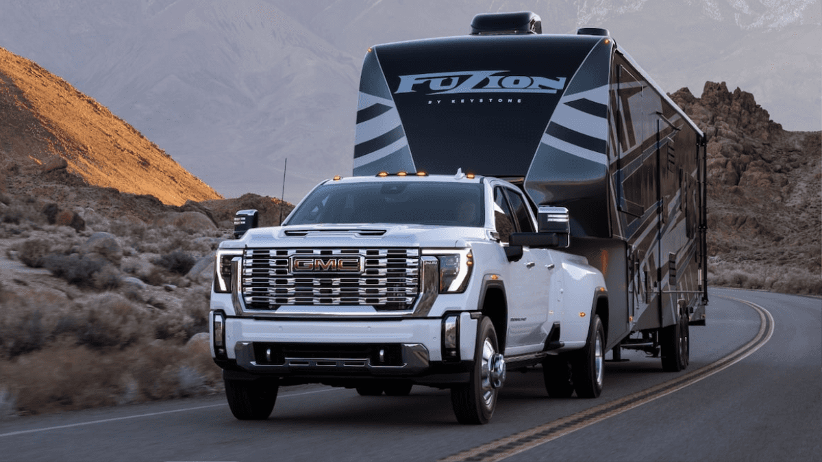 A white 2025 GMC Sierra 3500 hauling a trailer while driving down the road in a desert