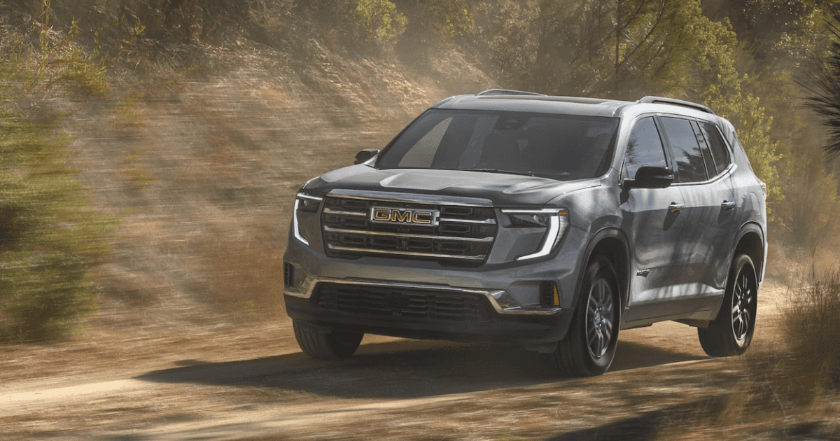 A gray 2025 GMC Acadia driving quickly over a dirt road