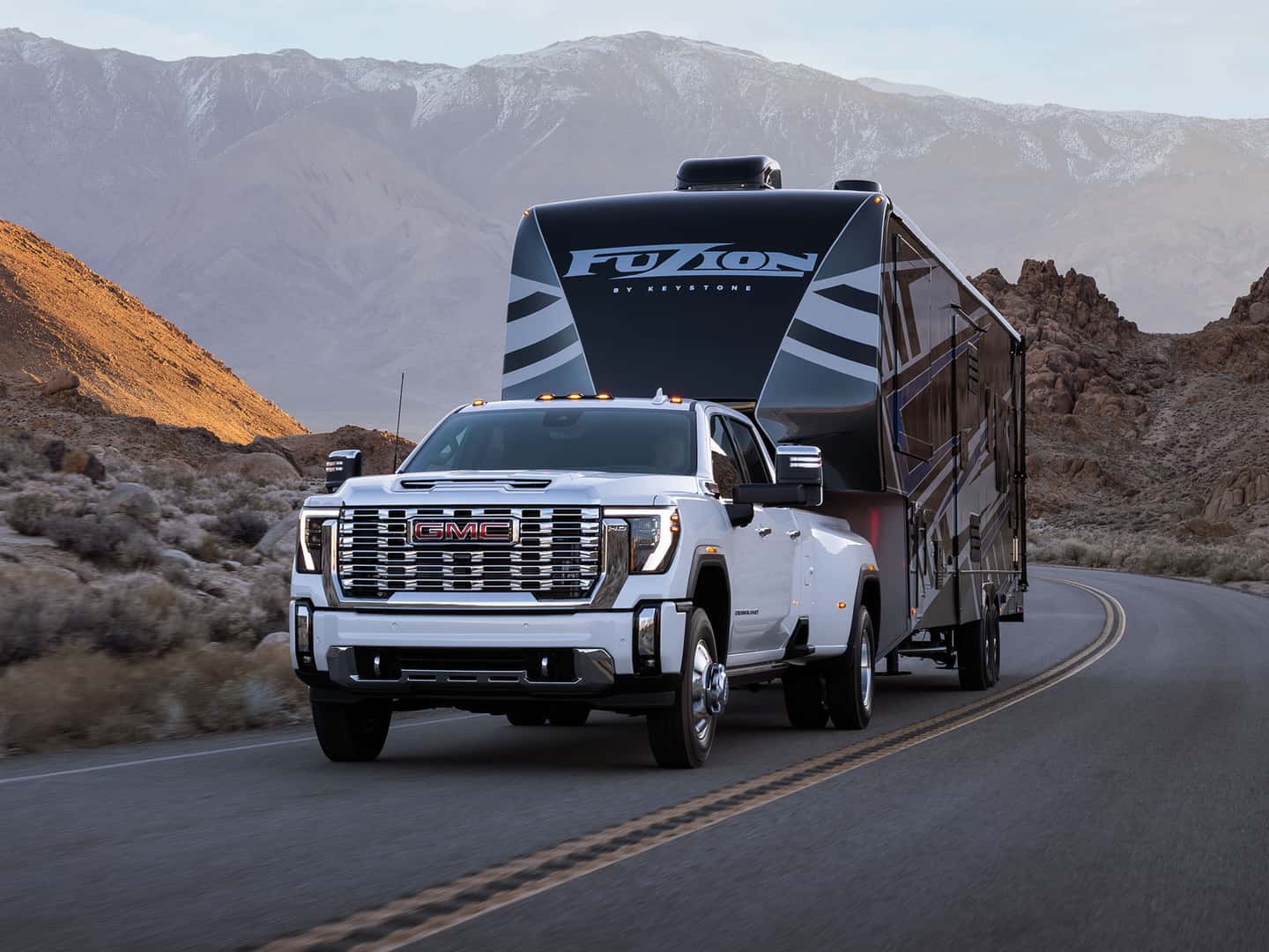 A white 2025 GMC Sierra HD with a trailer driving on a road through a desert