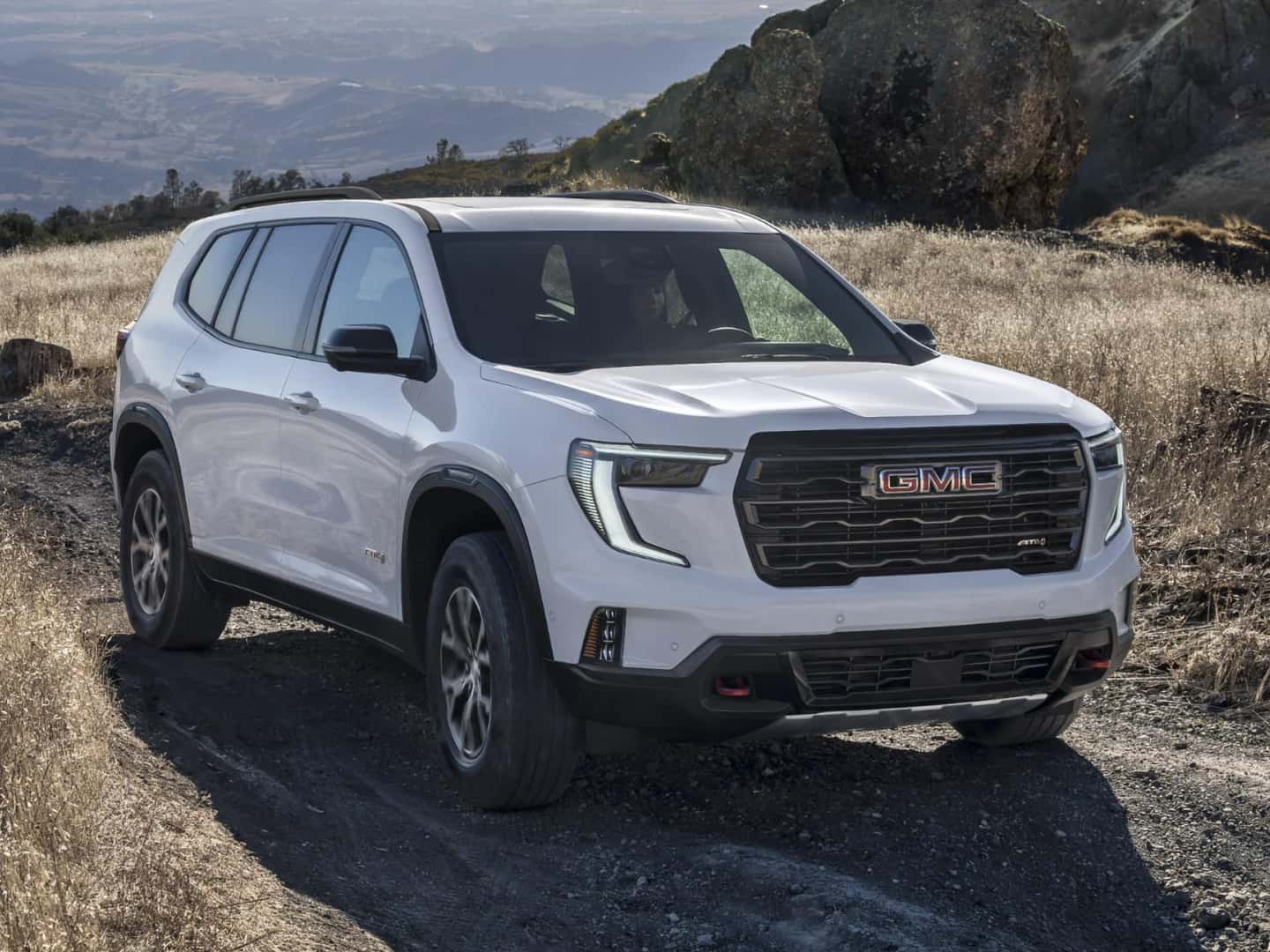 A white GMC Acadia driving on a dirt road through a field