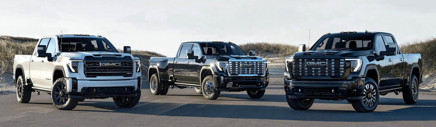 Three GMC Sierra 2500 HD pickup trucks (two black and one white) parked in the middle of a road