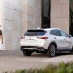 A rear view of a silver Buick Envision, parked by a building as a man wearing sunglasses walks away from it