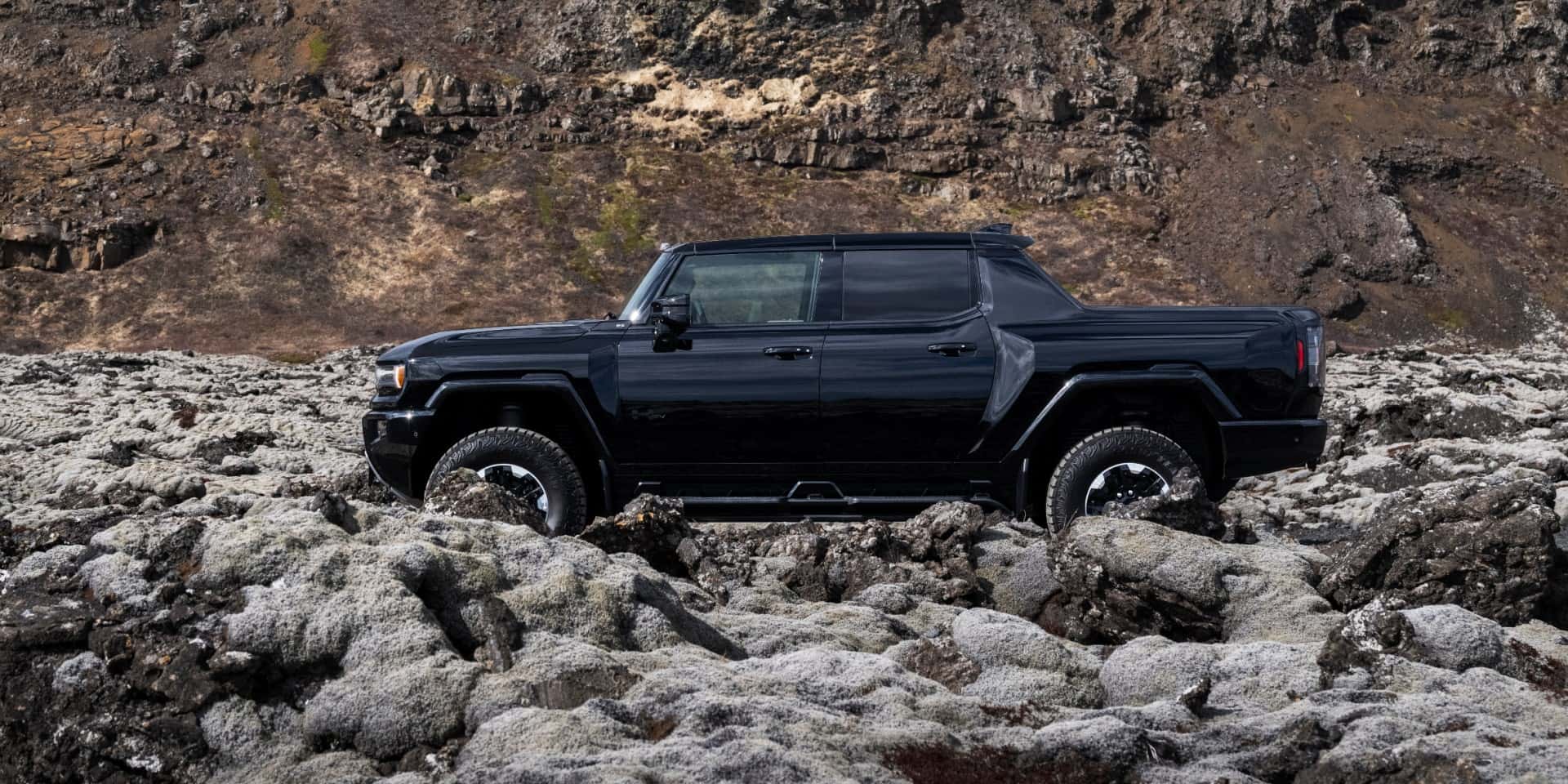 A black GMC Hummer EV driving over rocky terrain