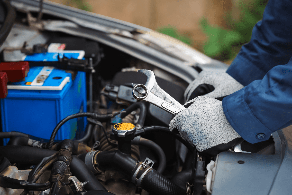A close up of an engineer's hands, holding a wrench as they repair a vehicle's engine