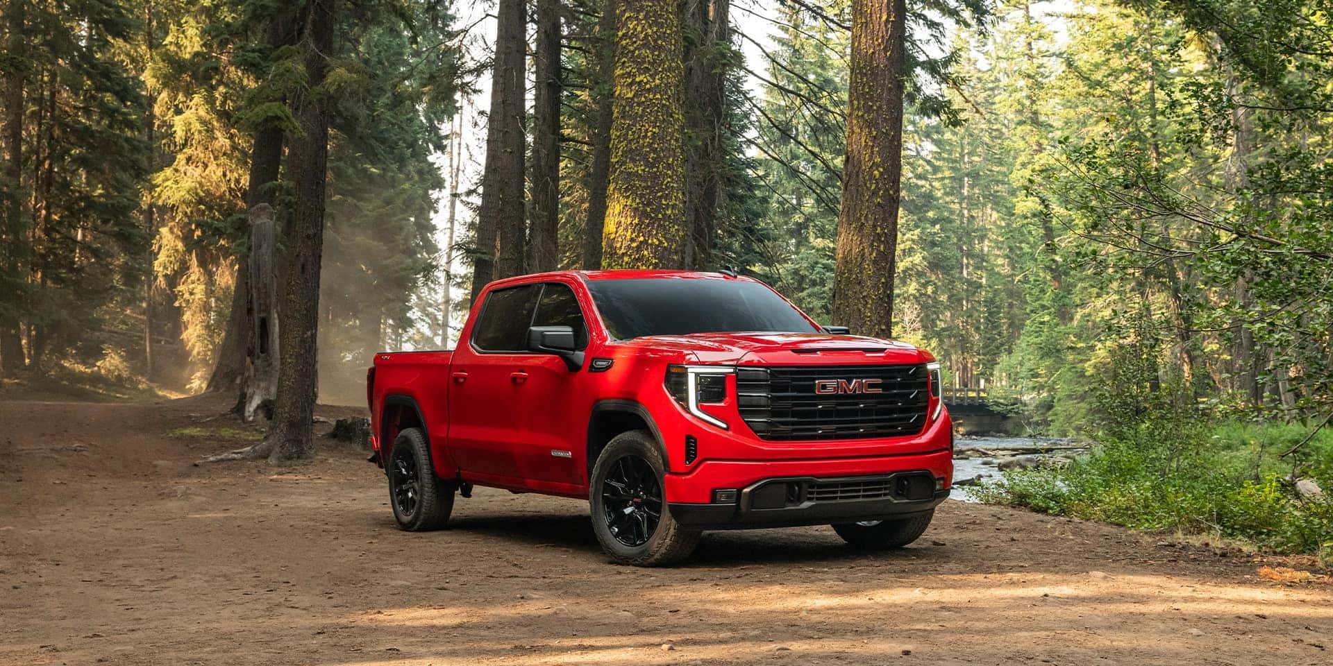 A red GMC Sierra 1500 driving on a dirt trail in a forest