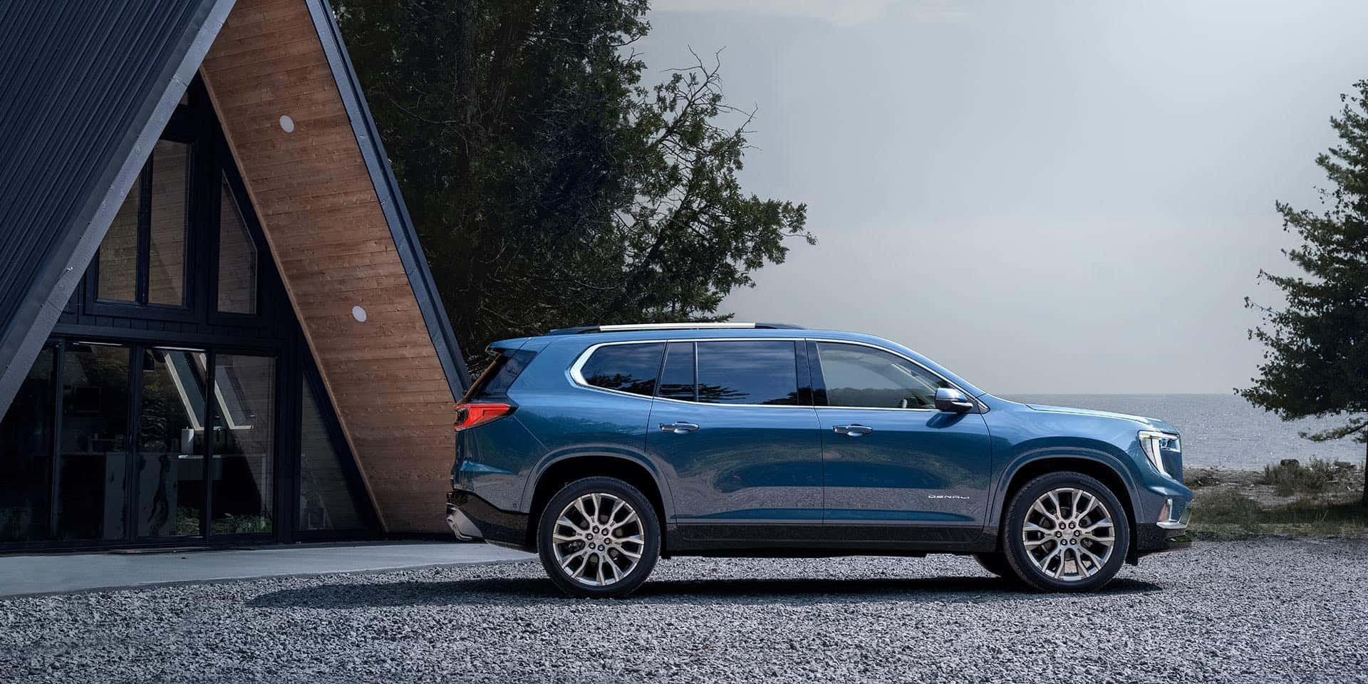 A blue GMC Acadia in profile, parked in front of a house near a beach