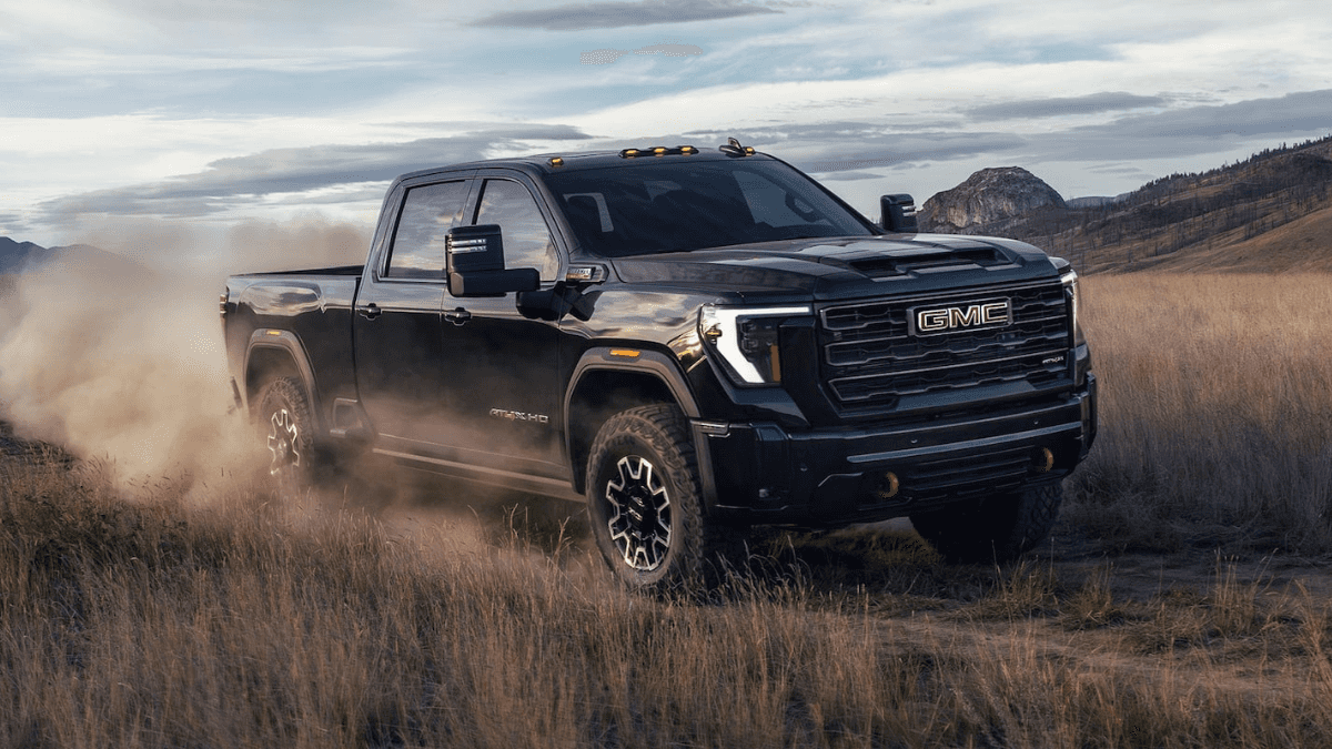A black GMC Sierra HD kicking up debris as it drives on a dirt road in a field