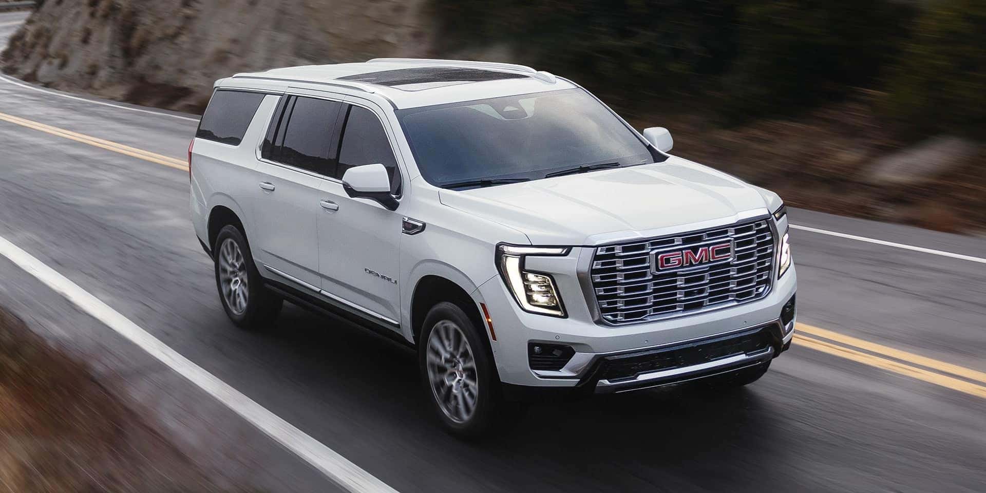 A white GMC Yukon driving around a hill