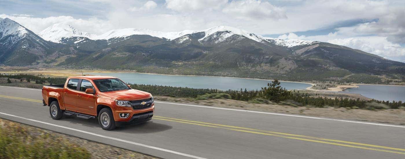 An orange 2016 Chevy Colorado Z71 is shown driving past a lake and mountains after visiting a used Chevy dealer.