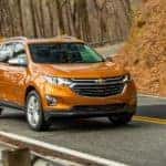 An orange 2018 Chevy Equinox is shown driving on a winding road after leaving a used Chevy dealer.