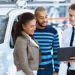 A salesman is shown speaking to a couple about how to sell their car.