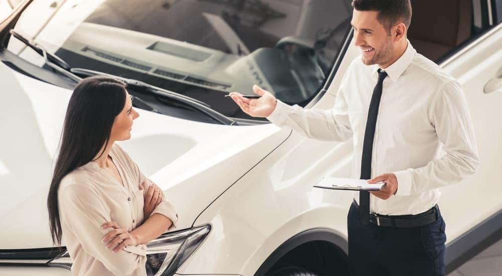 A salesman is shown speaking to a customer next to a white SUV.