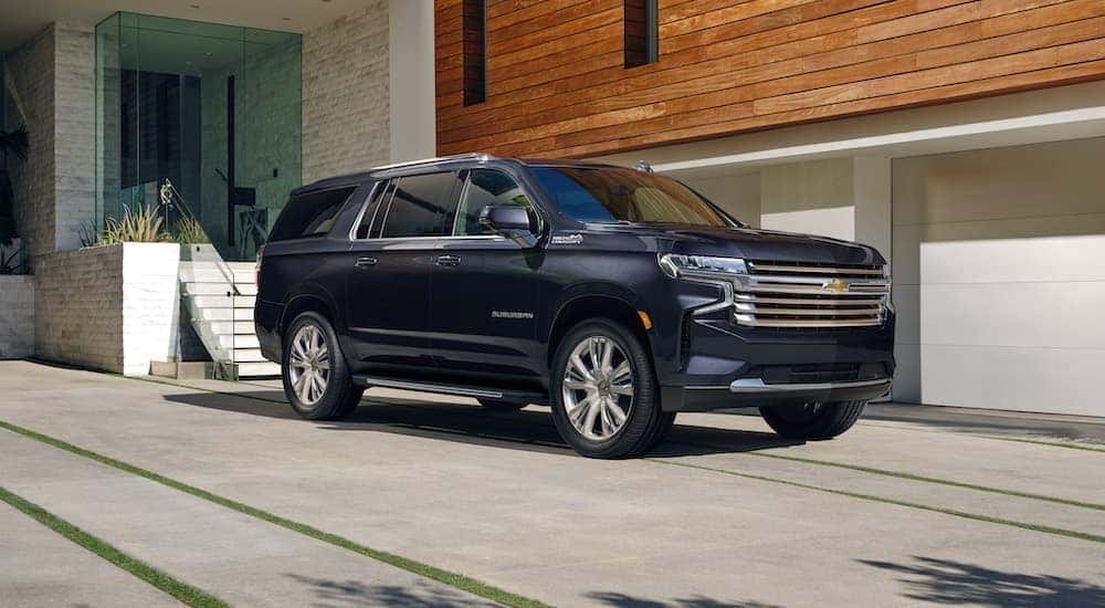 A blue 2023 Chevy Suburban is shown from the front parked in front of a house.
