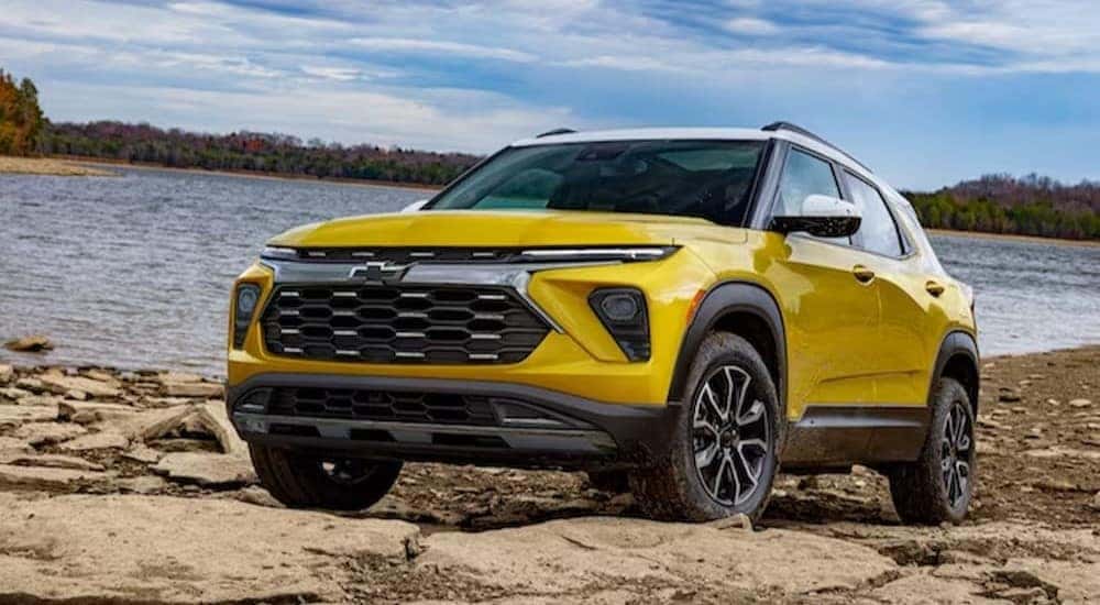 A yellow 2024 Chevy Trailblazer for sale is shown parked on rocks near a lake.