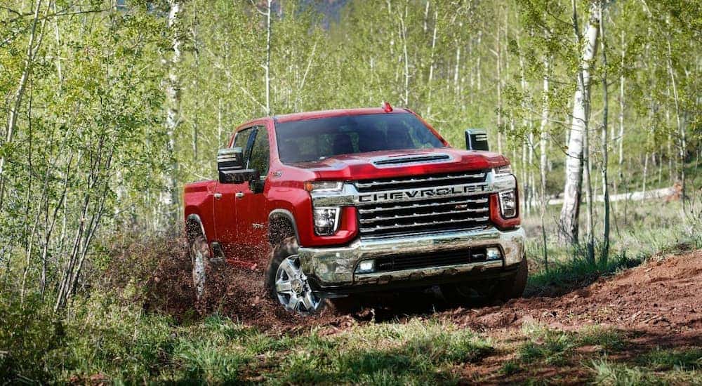 A red 2023 Chevy Silverado 2500 HD is shown off-roading on a forest trail.