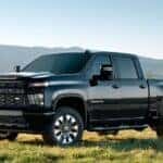 A black 2023 Chevy Silverado 2500HD Custom is shown parked in an open field.