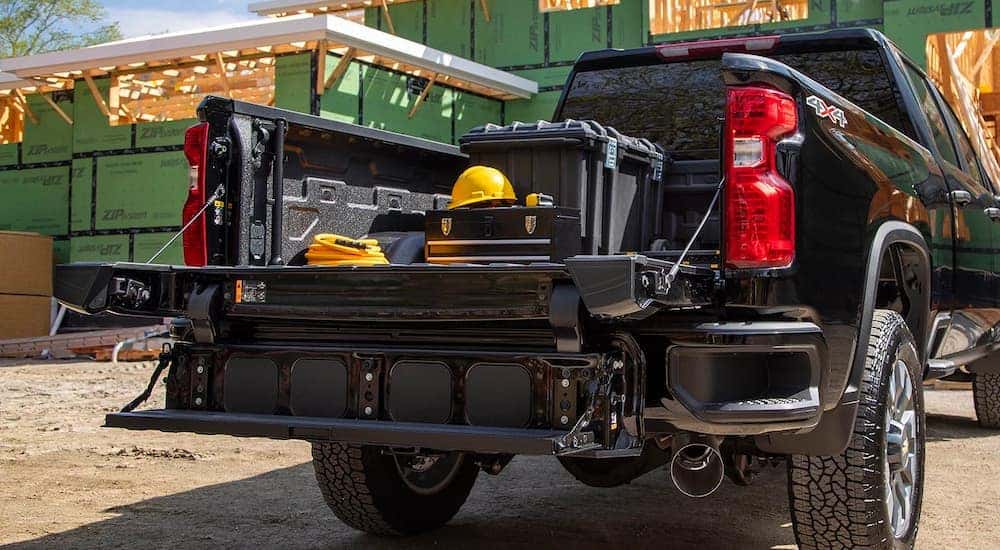 The open gate on a black 2023 Chevy Silverado 2500 HD for sale is shown at a construction site.
