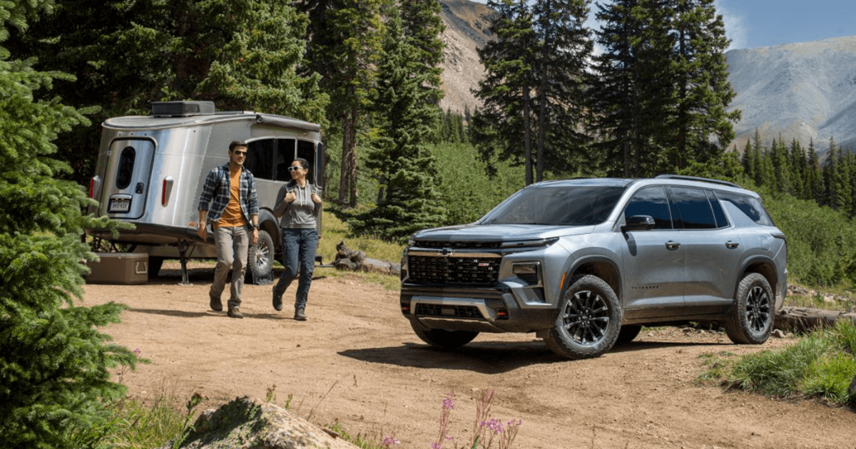 A 2025 Chevy Traverse parked on a dirt road on a hill, with a small trailer nearby